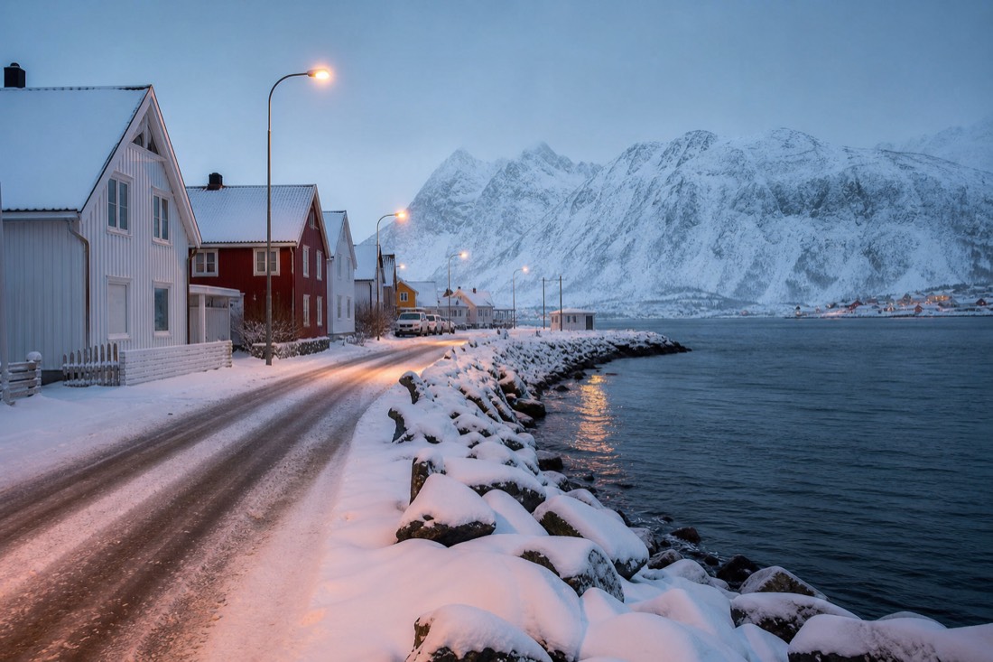 Empty snow-covered street of wooden houses in an Arctic Norwegian town lit by street lamps