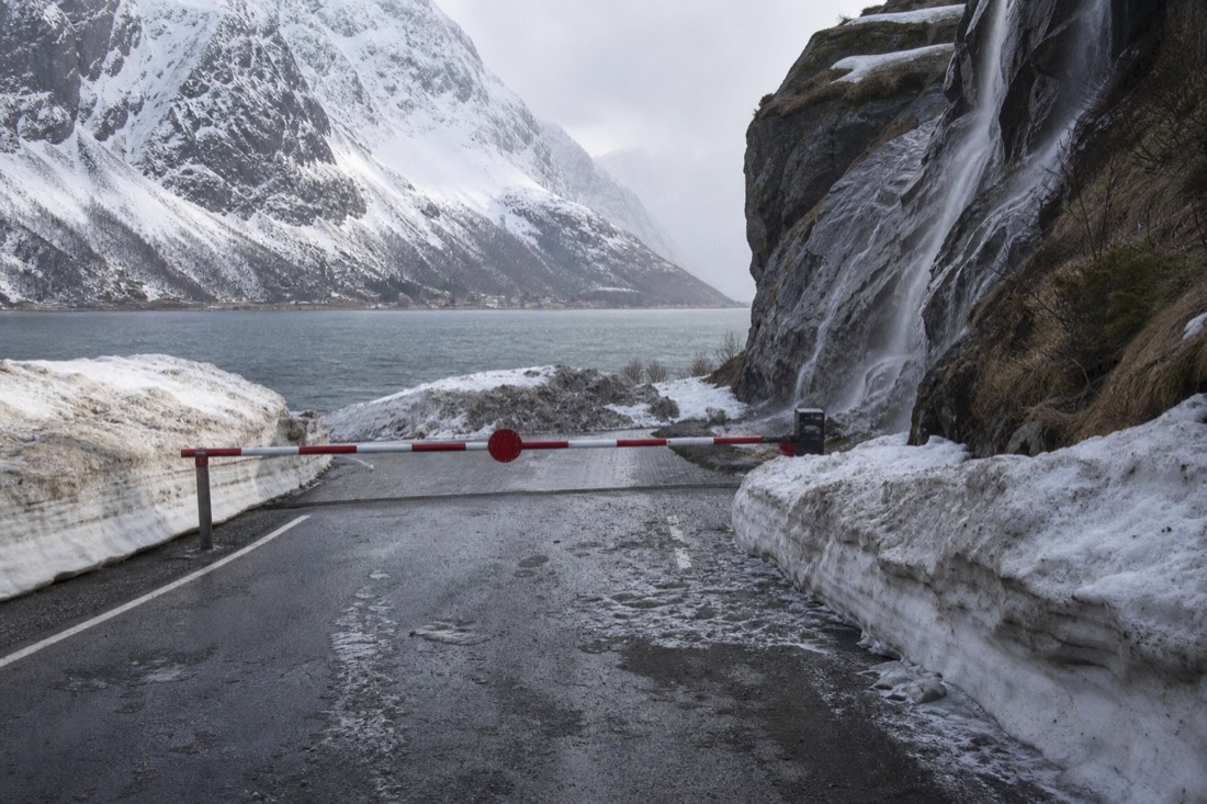 Snow-covered mountain road closed by a barrier with drifts banked high on either side
