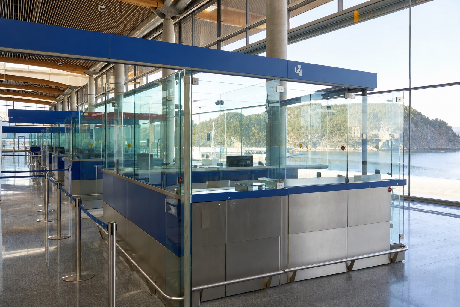 Passport control hall at a Norwegian airport with glass booths, blue signage and morning light through tall windows