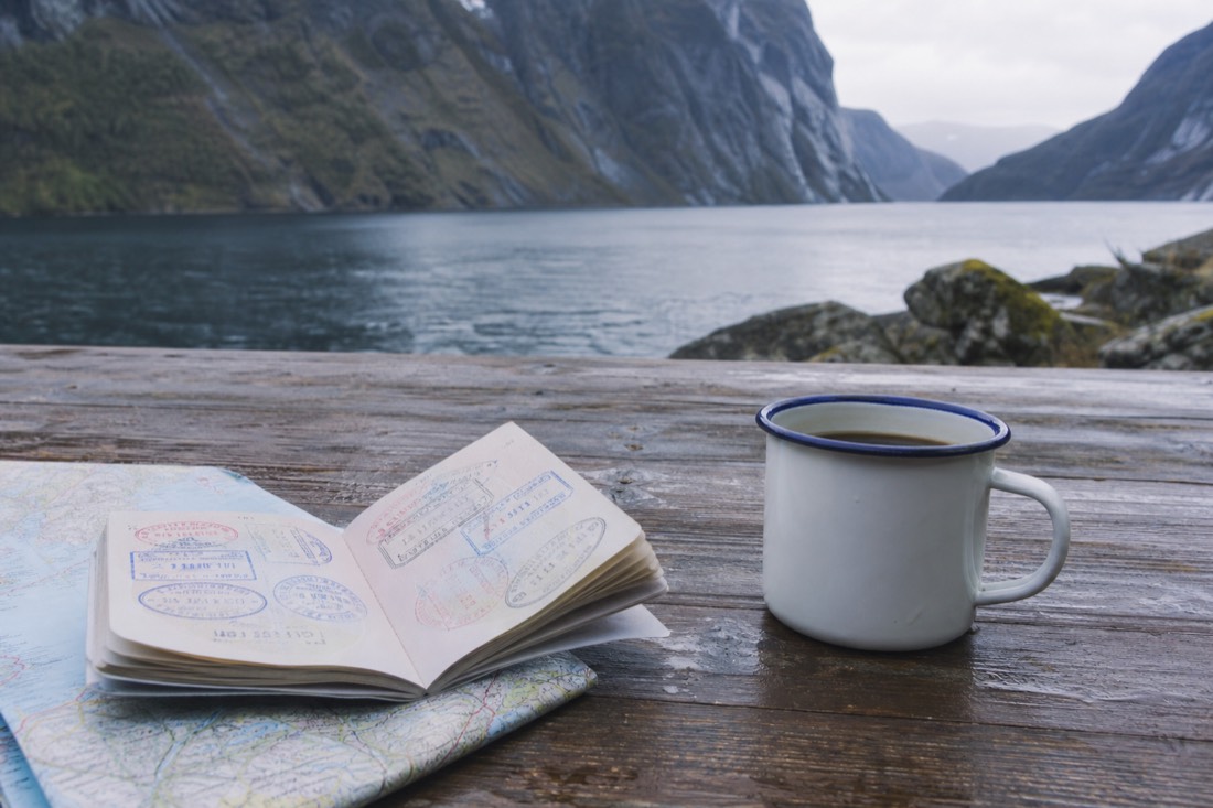 Open passport with entry stamps resting on a wooden table beside a folded map and a cup of black coffee