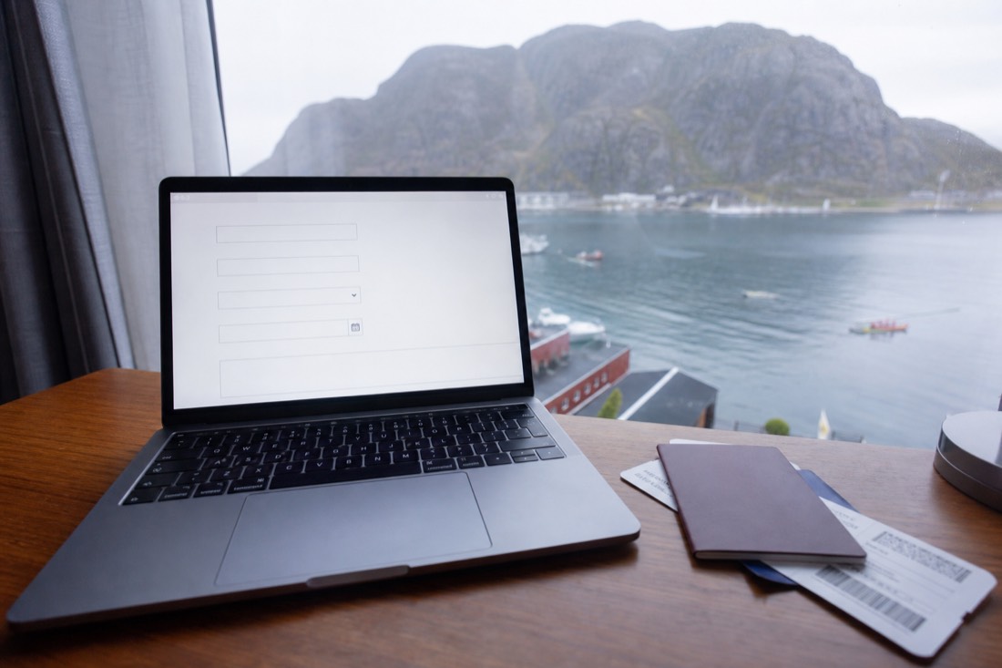Laptop open on a hotel desk showing a blank web form with a passport and boarding pass beside it