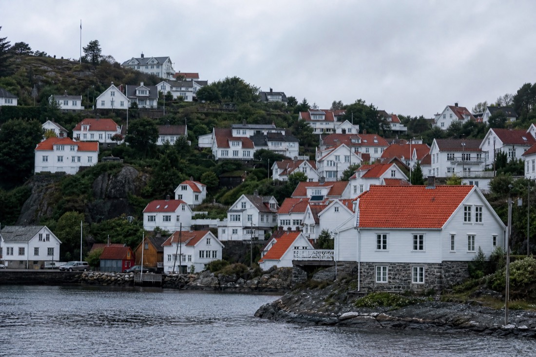 White wooden houses with red roof tiles climbing a hillside above a Norwegian harbour under grey sky