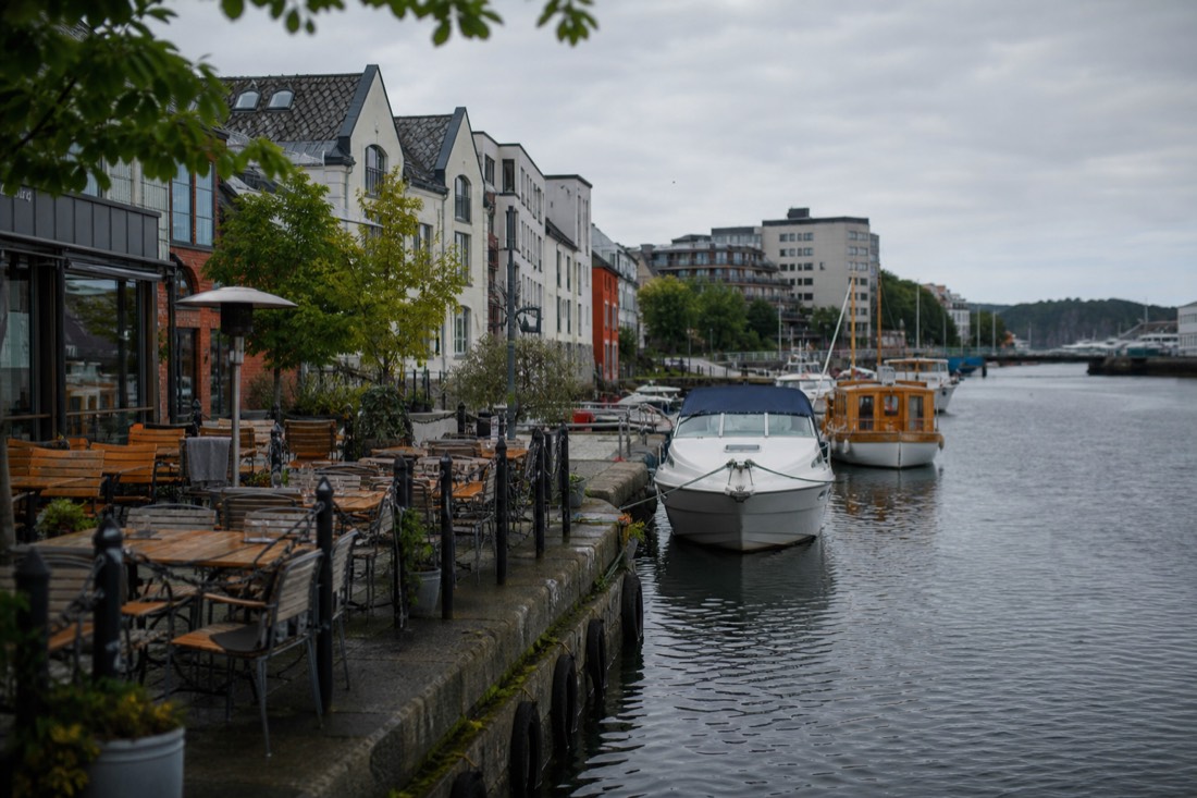 Harbourfront restaurant terraces with wooden tables facing moored boats in a small Norwegian city