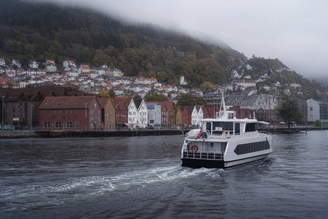 Wooden gabled warehouse fronts along a Bergen quay with a fjord boat departing in the foreground