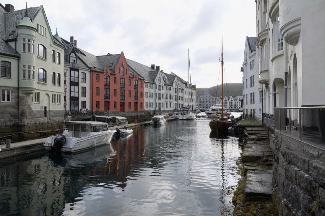 A narrow Norwegian harbour canal lined with ornate pastel buildings and small boats under a bright overcast sky