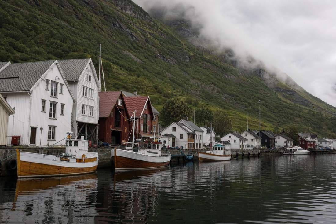 Leaning wooden gabled merchant houses along a working harbour front with green mountains rising directly behind