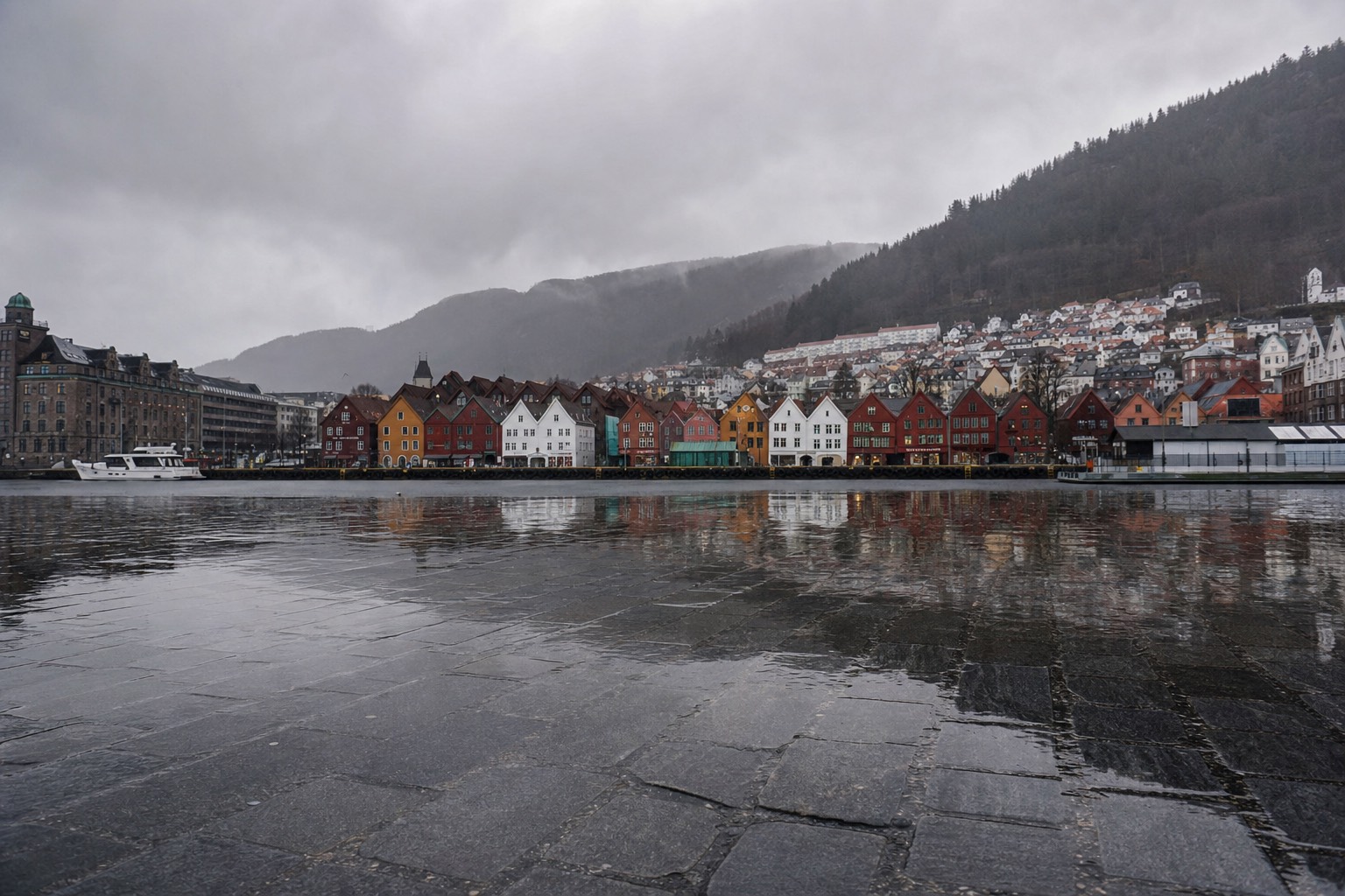 Rain falling on Bergen's coloured wooden wharf houses reflected in wet cobblestones under heavy grey cloud