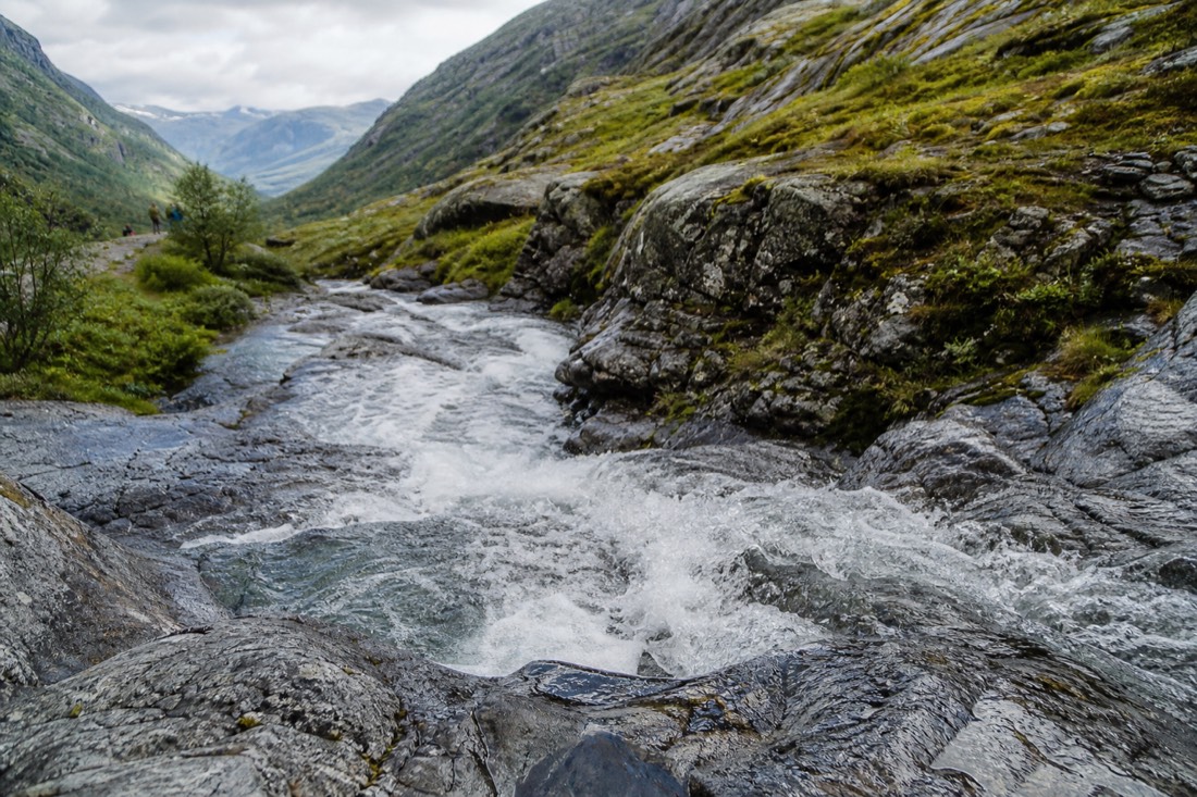 Clear mountain stream running over grey rock beside a Norwegian hiking path with green moss on the banks