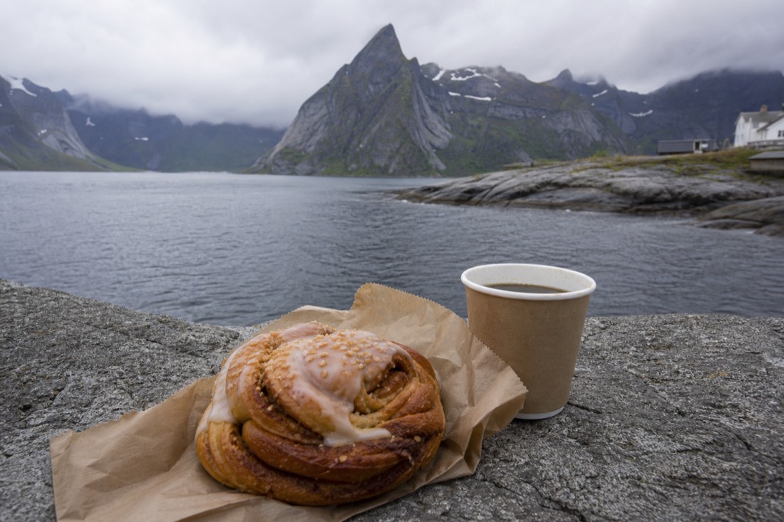 Large Norwegian cinnamon bun on parchment beside a paper coffee cup on a bakery counter
