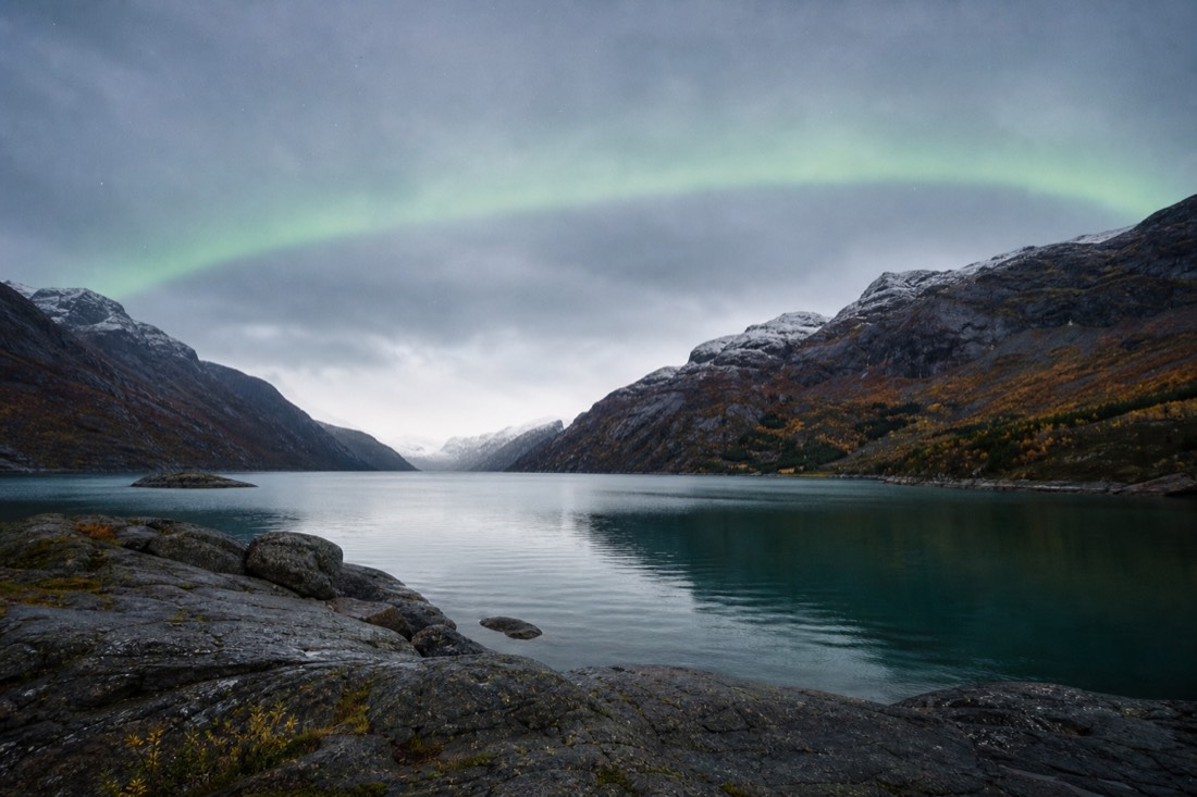 Faint green aurora band over an Arctic fjord in early autumn with snow only on the high peaks