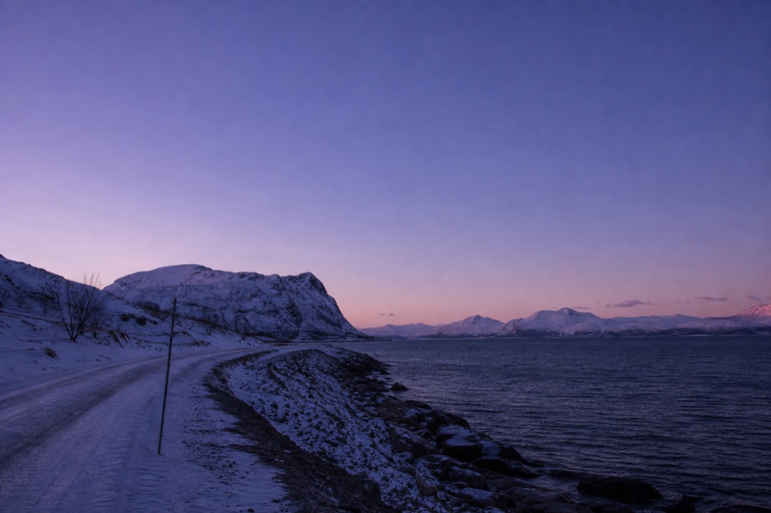 Snow-covered Arctic road at dusk in March with clear violet sky above dark ridgelines