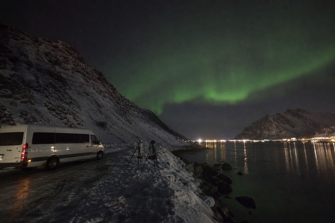 Minibus parked on a snowy roadside at night with tripods set up and green light overhead