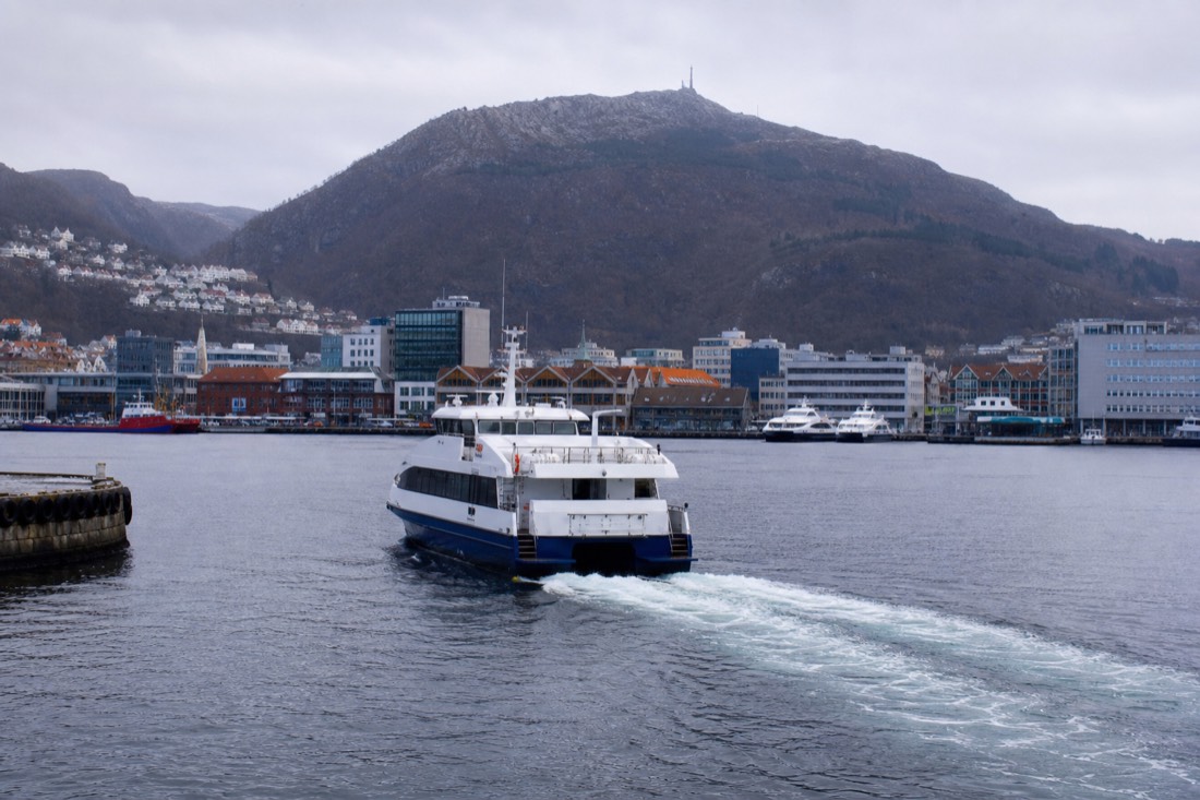 A fjord cruise boat leaving Bergen's Dreggekaien pier on grey-blue morning water