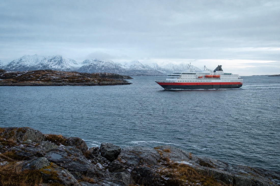 The Hurtigruten coastal ship sailing past snow-dusted islands under a pale arctic sky