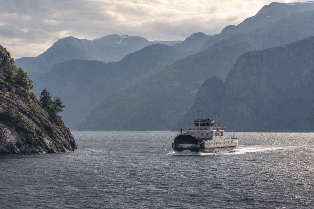 A scenic ferry crossing Sognefjord with layered mountain ridges fading into morning haze