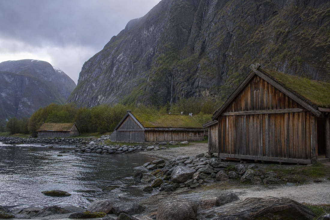 Timber longhouses of a reconstructed Viking village at Gudvangen beneath steep fjord cliffs