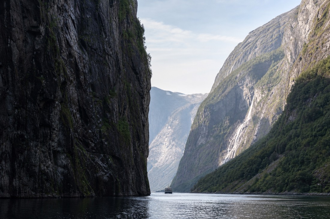 A fjord cruise boat dwarfed by the narrow cliff walls of Naeroyfjord on a clear morning