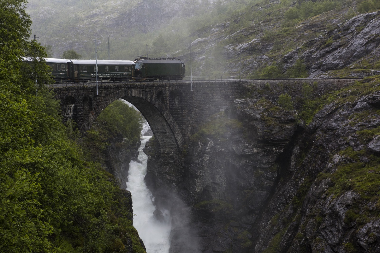 The Flam Railway crossing a stone bridge above a gorge with a waterfall thundering beneath