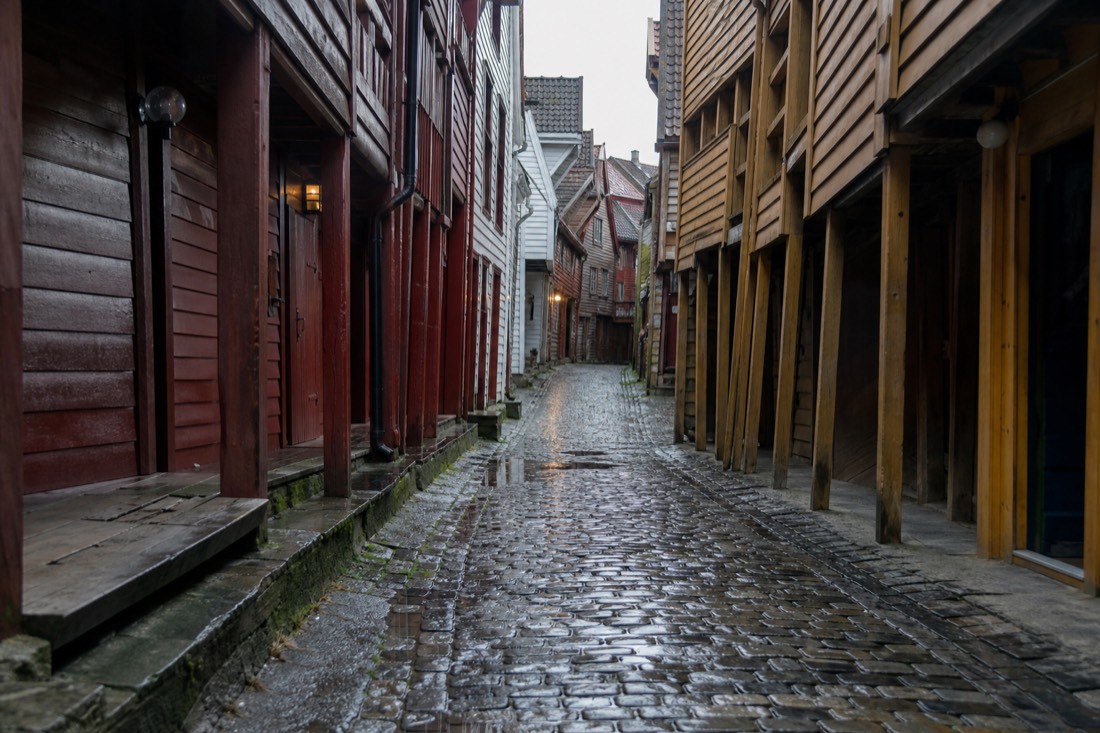 Cobbled alley between leaning wooden gable buildings in Bergen's old wharf district on a wet day