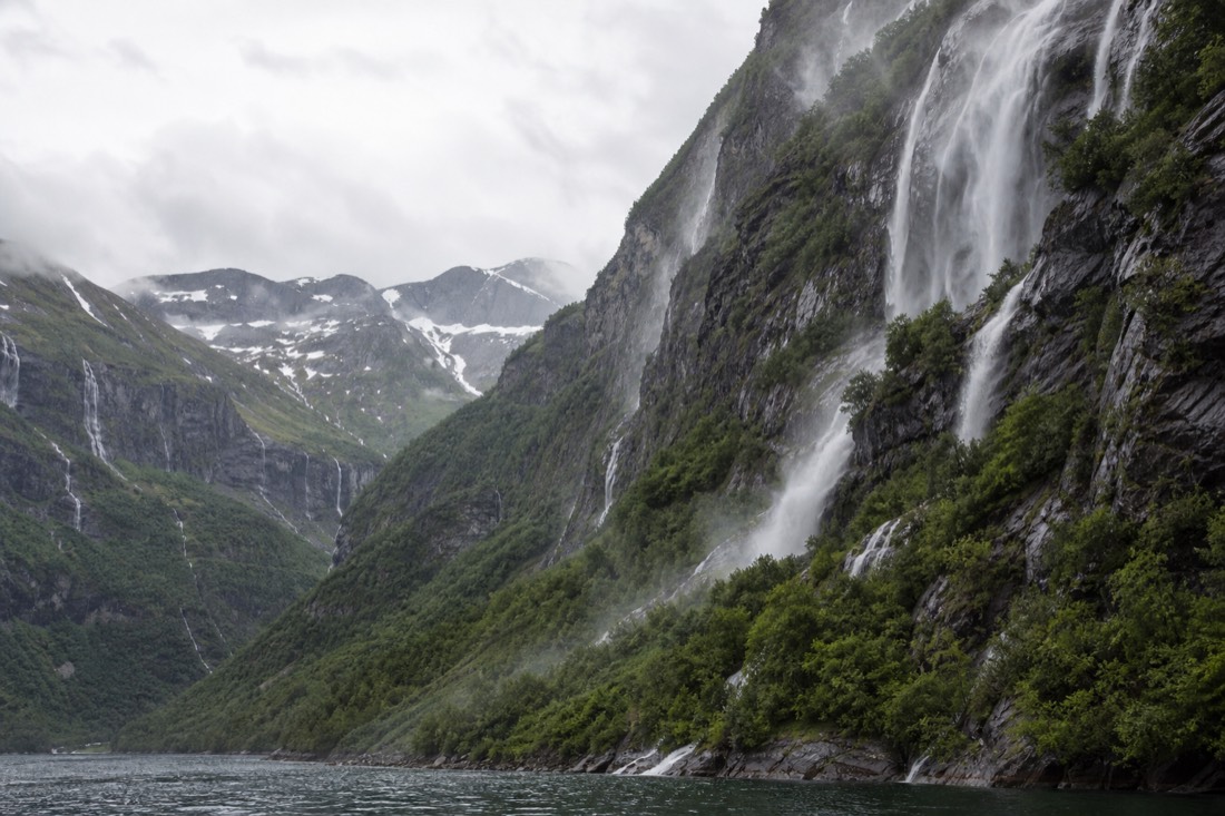 A green fjord valley in early June with waterfalls running high and patches of snow on the ridges above