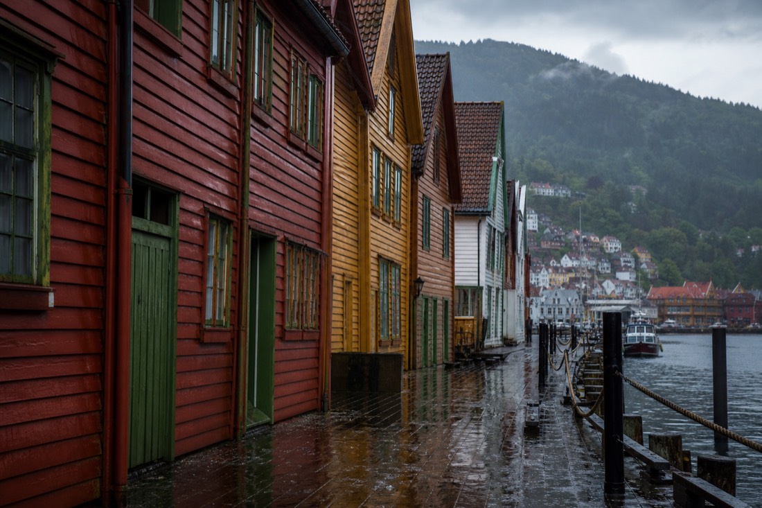 Rain-slicked wooden wharf buildings in Bergen with umbrellas and reflections on the cobbles