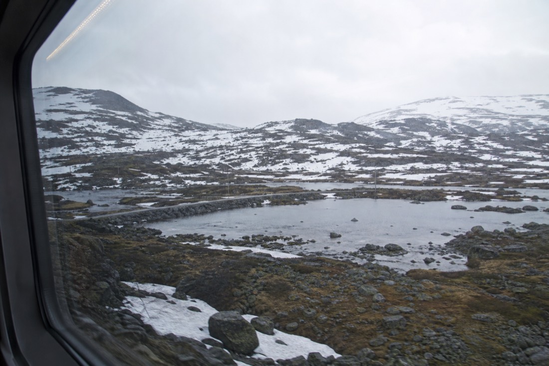 Train carriage window view of a snow-lined Norwegian mountain plateau on the Oslo to Bergen line