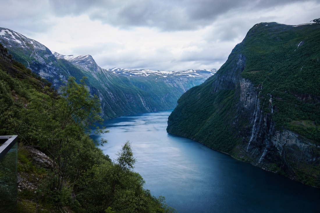 Narrow blue fjord seen from a viewing platform with steep green slopes falling to the water