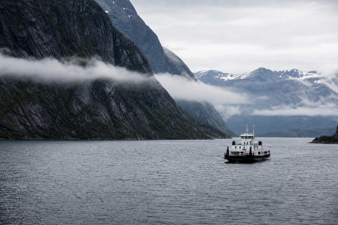 Small car ferry crossing a wide fjord with cloud sitting halfway down the mountainsides