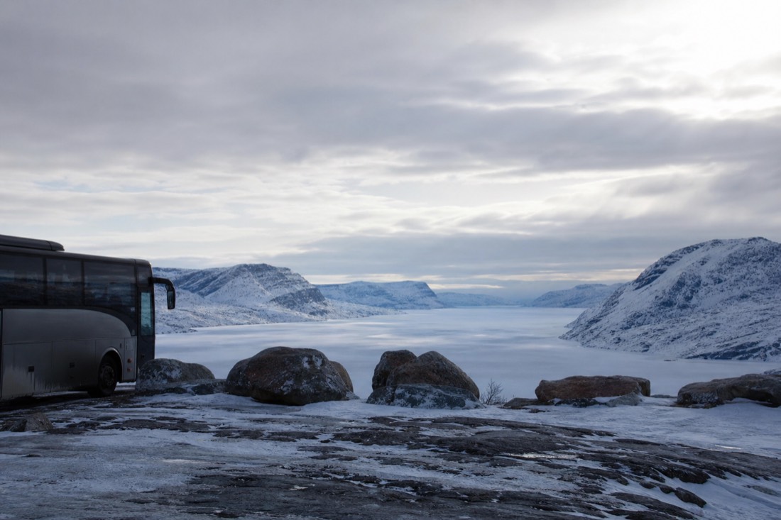 Coach parked at a snowy Arctic viewpoint with passengers looking out over a frozen valley