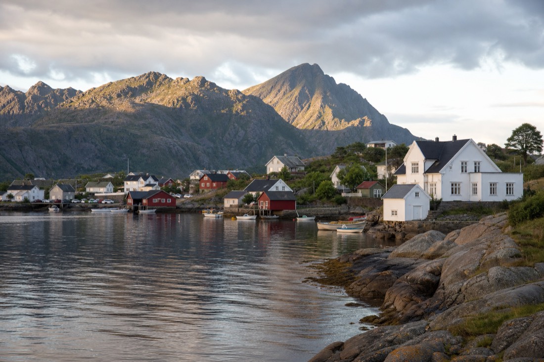 Late evening sunlight on a Norwegian fjord village with boats moored and mountains still lit