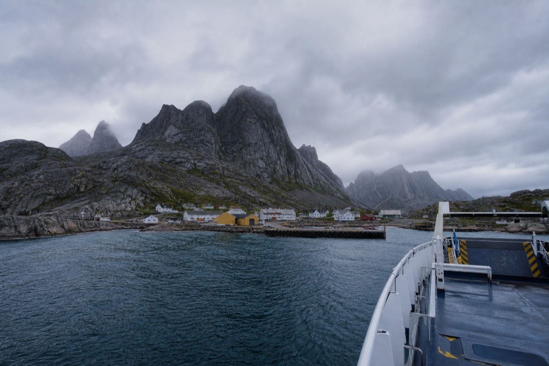 Car ferry approaching a small Arctic harbour with granite peaks rising behind the quay