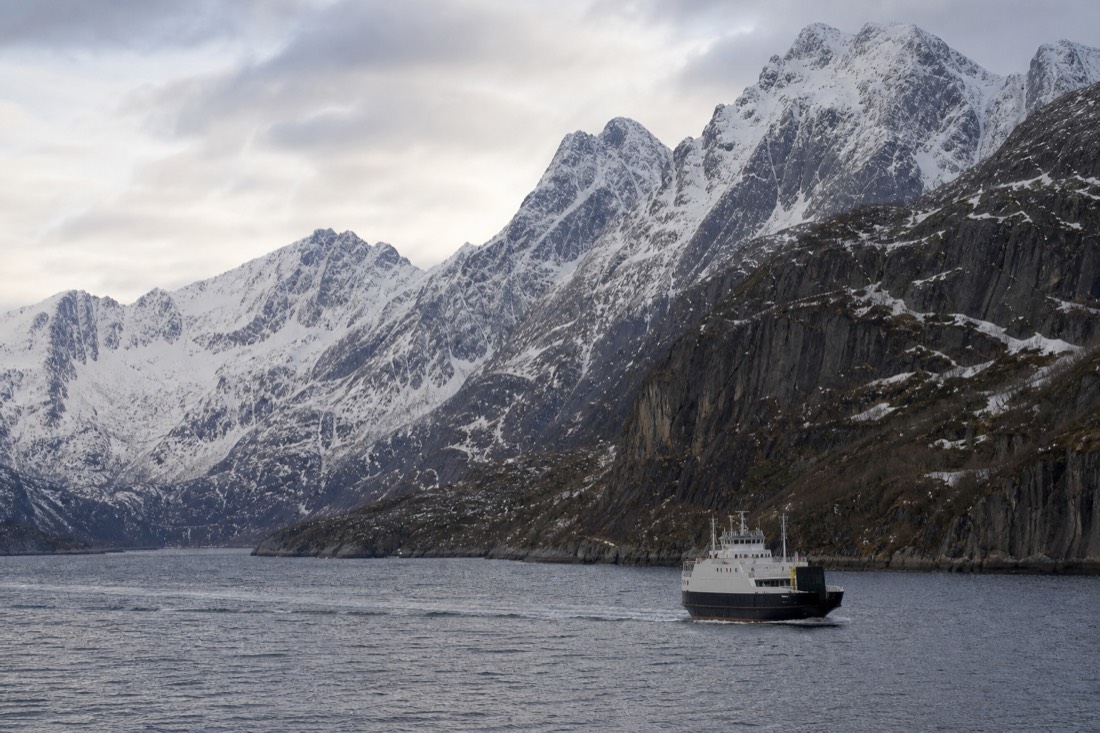 Coastal ship sailing past steep snow-covered mountains on a calm northern Norwegian sea