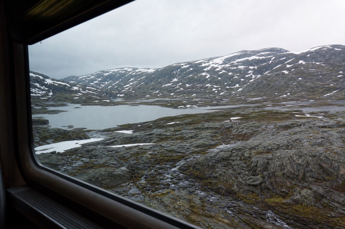 Snow-patched high mountain plateau seen from a train window with a small lake and no trees in sight