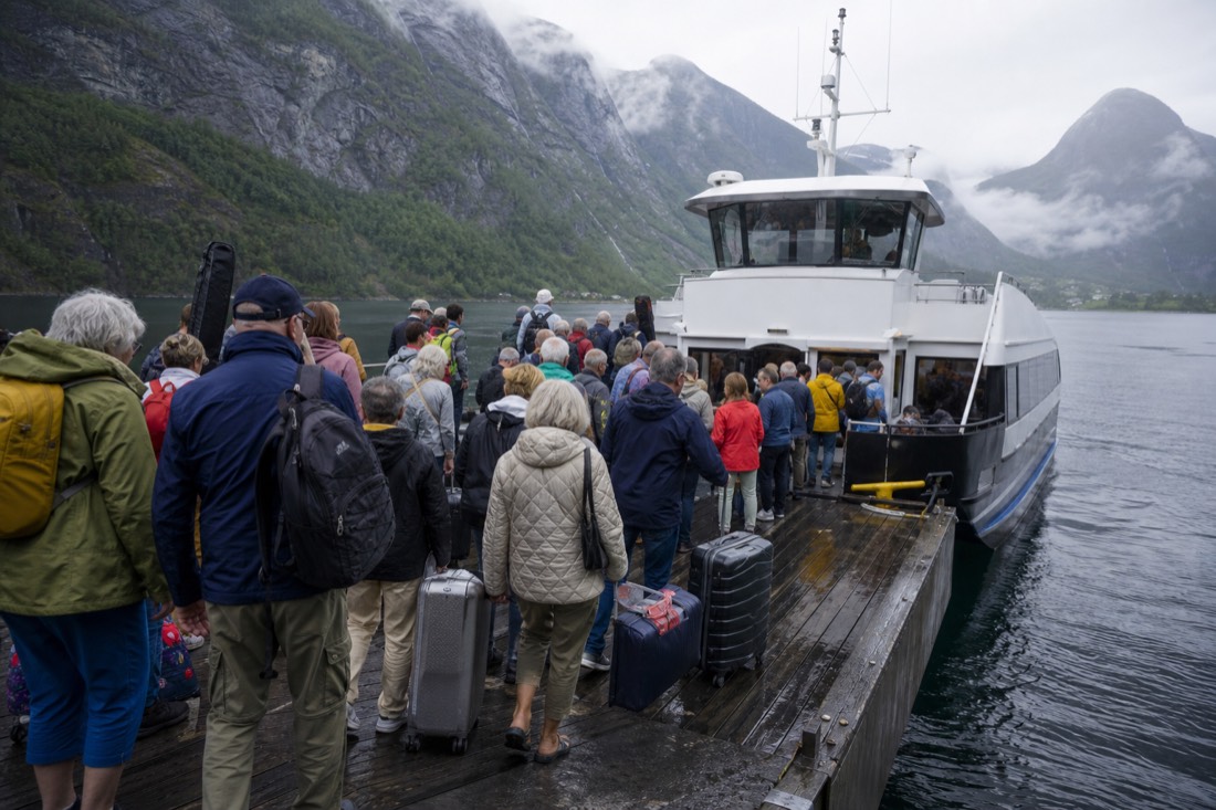 Crowded summer fjord pier with a white sightseeing boat boarding passengers beside stacked luggage