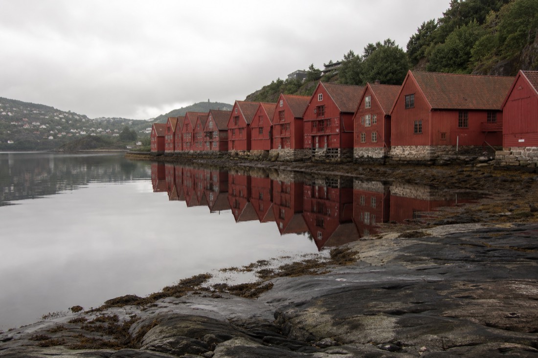 Red timber houses along Bergen's Bryggen wharf reflected in still harbour water under grey sky