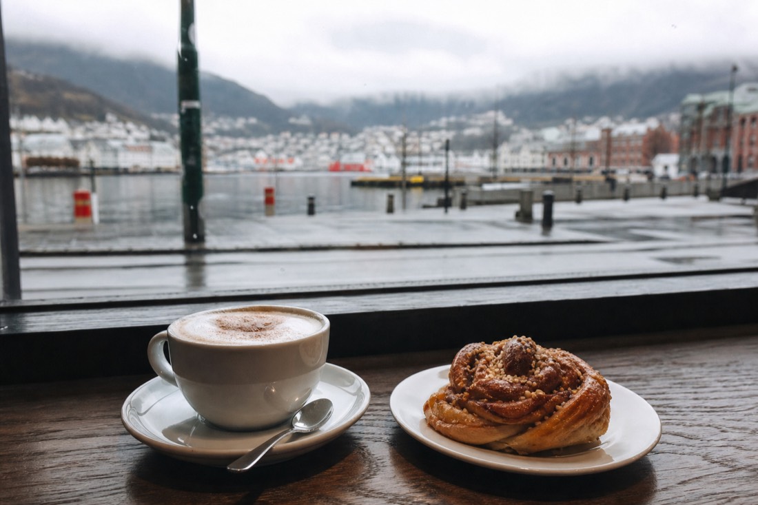 Cafe table with coffee and a cinnamon bun beside a window looking onto a Scandinavian city street