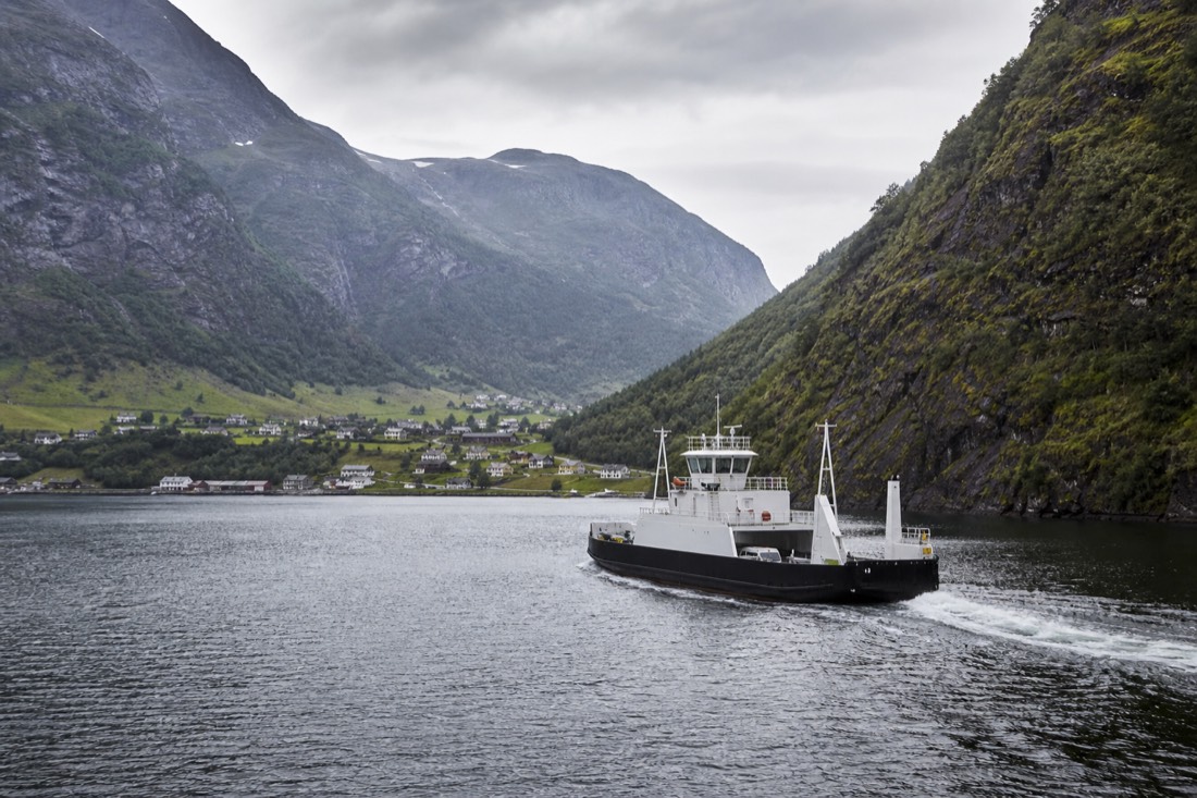Small car ferry crossing a calm fjord between steep green slopes with a village on the far shore