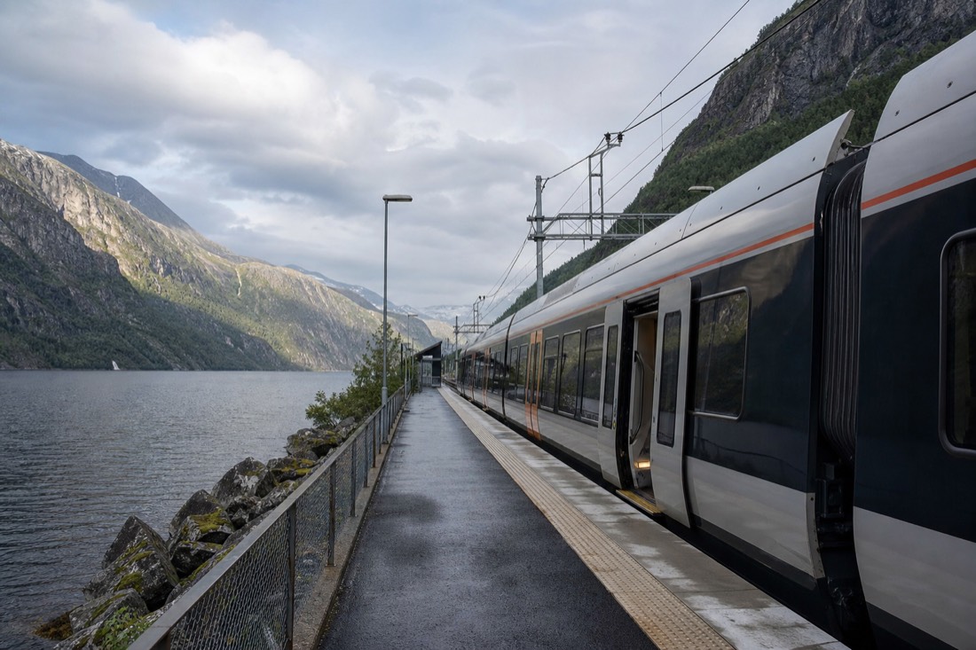 A modern Norwegian train platform with level boarding onto a carriage beside a fjord in soft afternoon light