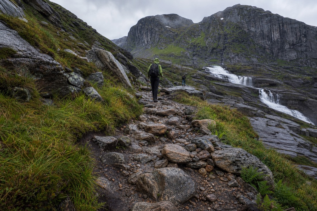 A rocky uneven mountain trail in Norway climbing between boulders with hikers using poles on the ascent