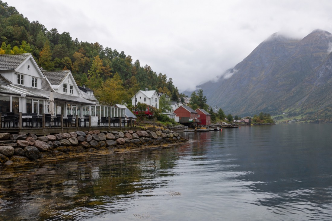 A quiet fjordside village with wooden houses, a small hotel terrace and a jetty on still water