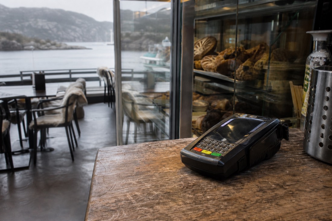 Contactless card terminal on a wooden counter in a small Norwegian cafe with pastries behind glass