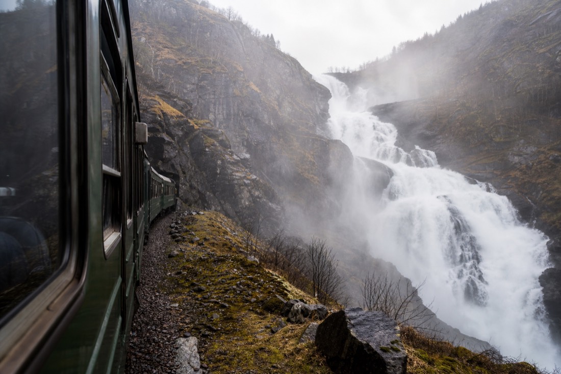 Green train carriage stopped beside a thundering waterfall on a steep mountain railway line