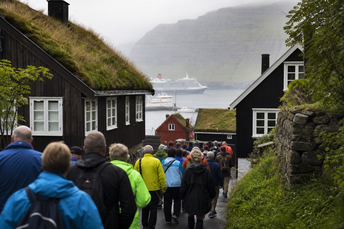 Cruise passengers walking a narrow village street between wooden houses on a crowded summer day