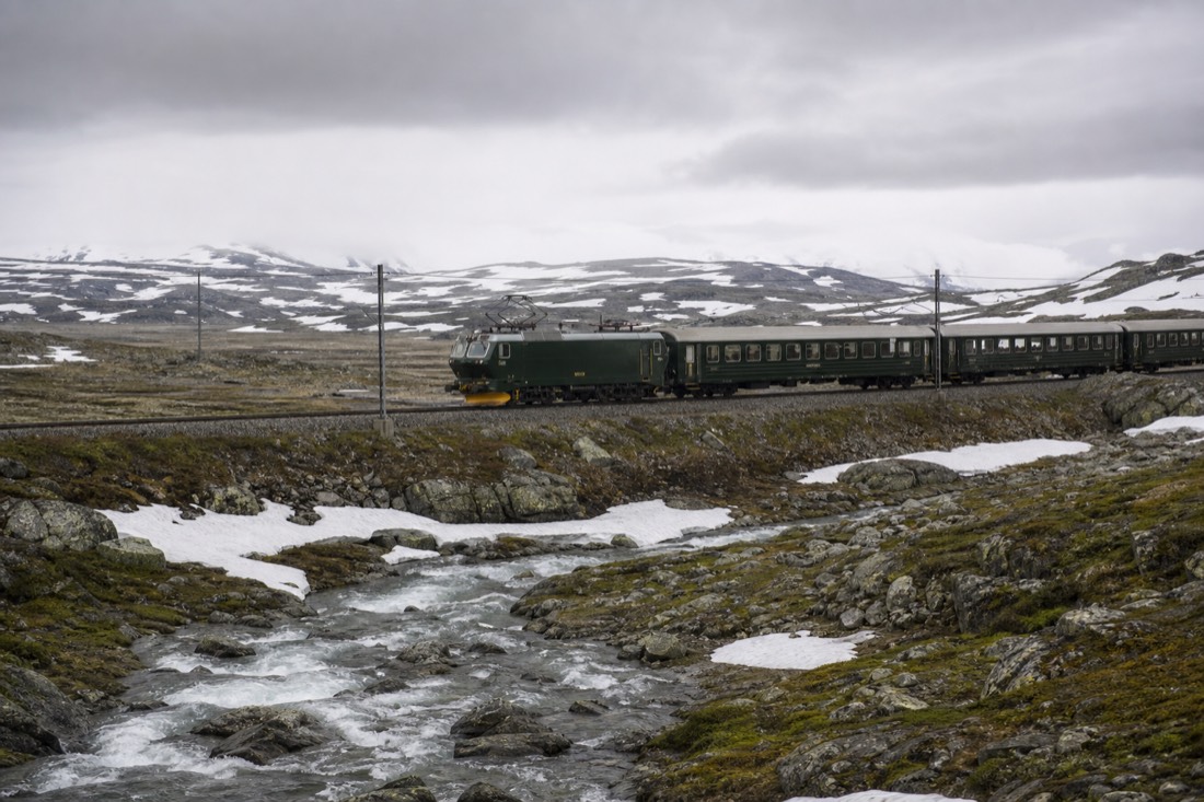 Train crossing an open snow-patched mountain plateau under wide grey sky with no buildings in sight