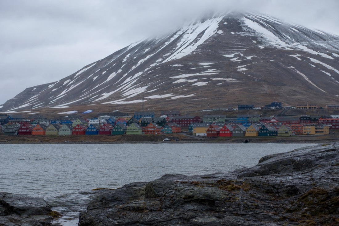Colourful timber houses of Longyearbyen below a snow-streaked brown mountain under flat Arctic light