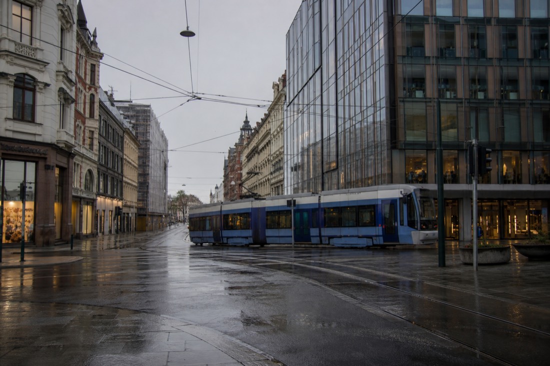 A tram crossing a city street in central Oslo with 1900s facades and a modern glass building side by side