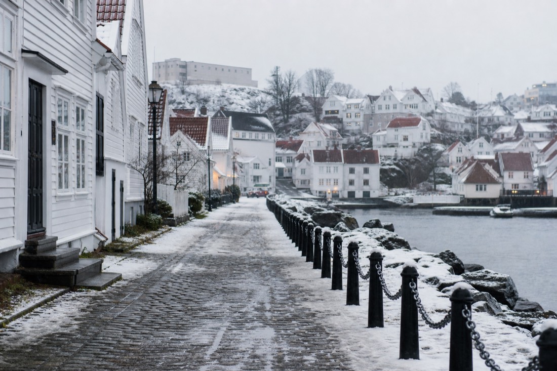 Snow-covered cobbled street in a Norwegian town with icy pavement and warmly dressed figures walking